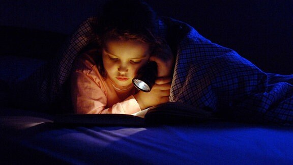 Kleines Mädchen liest im Bett mit einer Taschenlampe