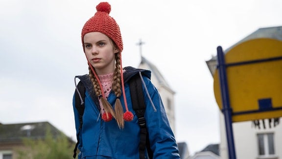Ein Mädchen mit Roter Mütze und blauer Jacke geht auf der Straße