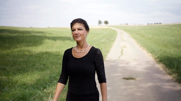 Sahra Wagenknecht spaziert in einem schwarzen Kleid einen Feldweg entlang.