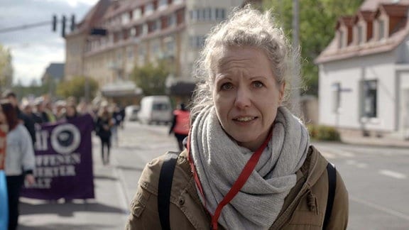 Eine Frau steht am Rande einer Demonstration.