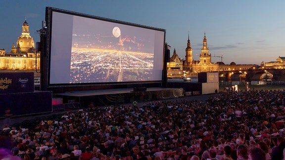 Zahlreiche Gäste der "Filmnächte am Elbufer" sitzen vor der Kulisse der Dresdner Altstadt vor einer Kinoleinwand