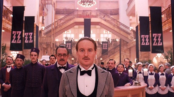 Szene aus dem Film "Grand Budapest Hotel": Mitarbeitende eines Hotels stehen in einer großen Empfangshalle und blicken in die Kamera