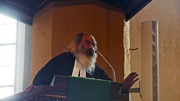 Lothar König, Jugendpfarrer aus Jena: Ein Mann mit Bart steht auf einer Kanzel in der Kirche und predigt.