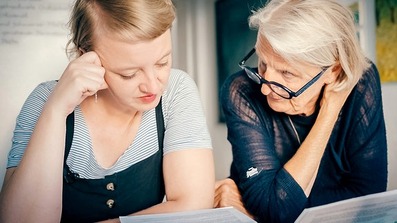 Eine junge Frau und eine ältere Frau mit grauen Haaren sitzen nebeneinander und sind im Gespräch.