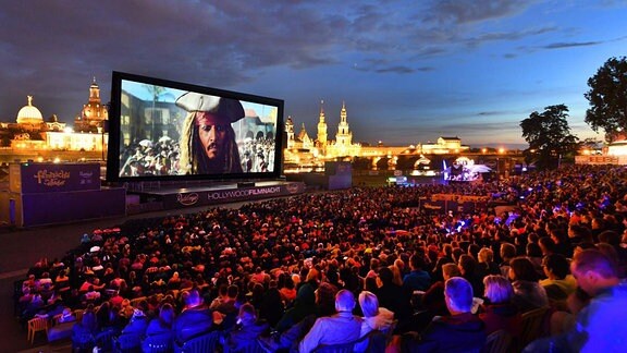 Eine große Kinoleinwand mit Publikum vor der nächtlichen Kulisse der Stadt Dresden