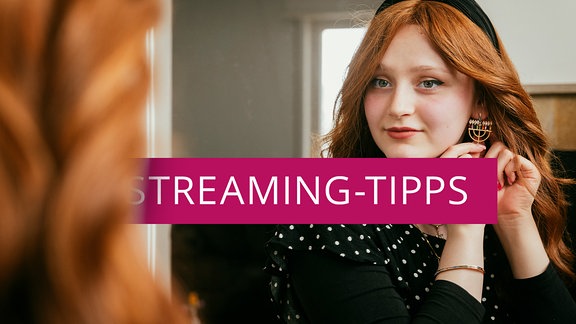 Eine Frau legt Ohrringe in Form eines Chanukkaleuchters an, davor der Schriftzug "Streaming-Tipps".