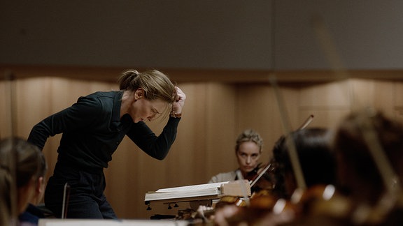 Schauspielerin Cate Blanchett im Film Tár als Dirigentin bei einer Probe im Konzertsaal.