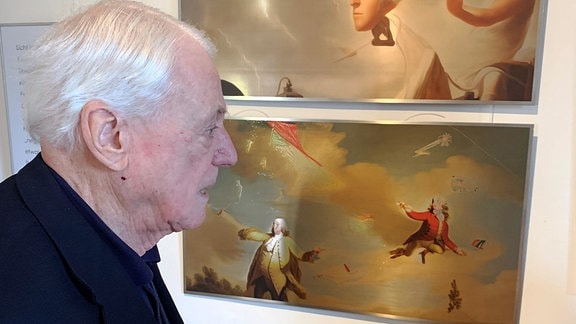 Alexander Kluge steht vor einer Wand mit mehreren Bildern.