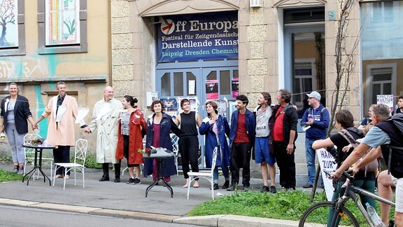 Mehrere Menschen stehen in einer Reihe vor einer Tordurchfahrt und halten sich an den Händen, um sich zu verbeugen.