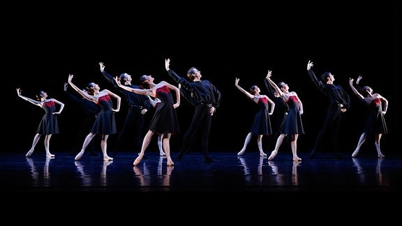 Eine Tanzgruppe auf der Theaterbühne: Synchron heben die Frauen die Arme und drücken den Rücken durch, währen die Männer sie halten.