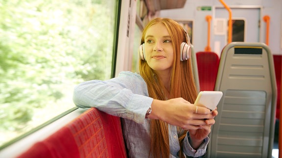 Eine junge Frau hört während einer Zugfahrt Musik über Kopfhörer.