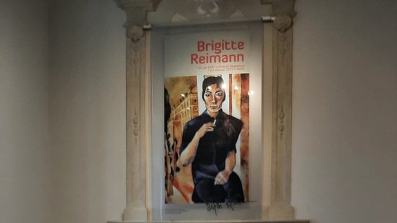 Blick in eine Ausstellung in Hoyerswerda, ein Schreibtisch, davor ein Stuhl, über einem Kamin hängt ein Palkat mit der Aufschrift "Brigitte Reimann".