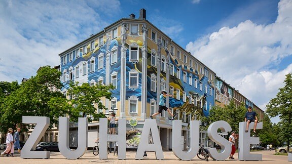 "ZUHAUSE" steht in großen dreidimensionalen Lettern auf einer Straße.