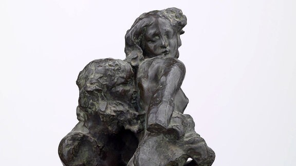 Foto einer dunkelgrauen Skulptur: Ein männlicher Körper ohne Beine und mit Bart hält einen weiblichen Körper hoch.