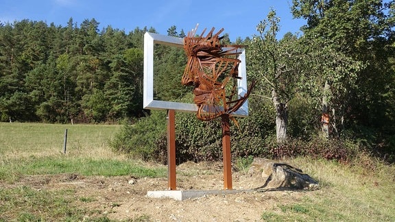 Kunstwerk auf dem Kunstwanderweg Kleinbreitenbach in Thüringen: ein übergroßer Bilderrahmen aus Eisen, in dessen Mitte sich ein aus Metallstreben geformtes Gesicht befindet