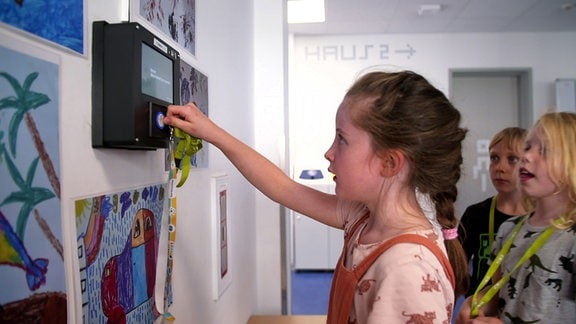 Ein Mädchen hält einen elektronischen Chip an ein Lesegerät, dahinter warten weitere Kinder
