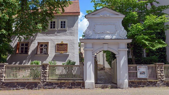 Das Schillerhaus mit barockem Eingangstor und grünen Bäumen in der Menckestraße in Leipzig 