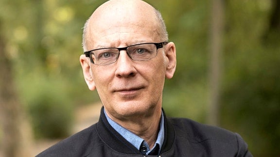 Porträt von Andreas Heidtmann: Ein Mann mit Brille steht in einem Park.