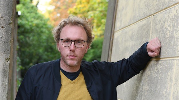 Ein junger Mann mit blonden Haaren lächelt freundlich.