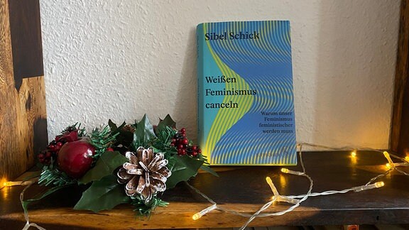 Das Buch "Weißen Feminismus canceln" steht neben einer Lichterkette und Weihnachtsdeko auf einem Regal.