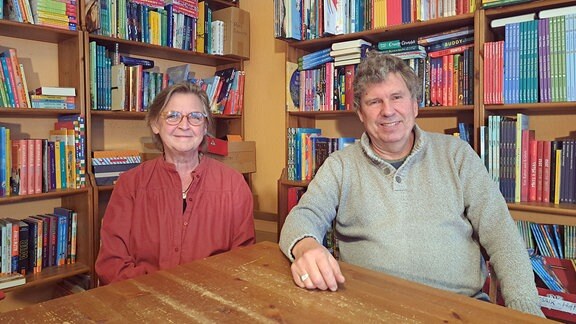 Eine Frau und ein Mann sitzen an einem Tisch, im Hintergrund sind Regale voller Bücher.