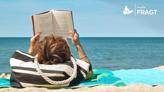 Eine Frau liest ein Buch am Strand.