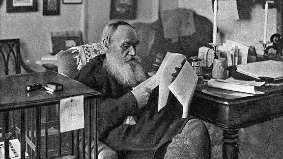 Leo Tolstoi sitzt in seinem Arbeitszimmer und liest einen Text.