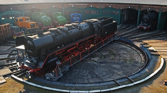 Eine historische Dampflokomotive steht auf der Drehscheibe vor dem Ringlokschuppen der Eisenbahnfreunde Traditionsbahnbetriebswerk Stassfurt. 