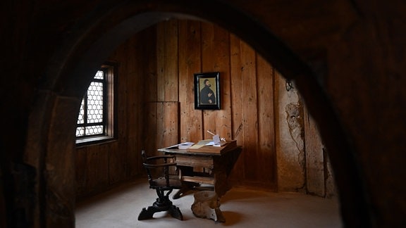 Die Lutherstube in der Wartburg, Blick in einen holzgetäfelten Raum, in dem ein Schreibtisch mit Stuhl davor steht. 