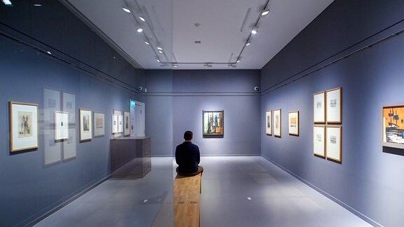 David Grube, Kurator und Kunsthistoriker der Lyonel-Feininger-Galerie, sitzt 2021 vor einem Gemälde.