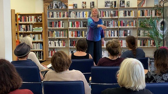 Aufnahme vom Märchen- und Sagenfest Meiningen 2023: Eine Frau steht vor einem Publikum in einer Bibliothek, hinter ihr ein Regal voller Bücher.