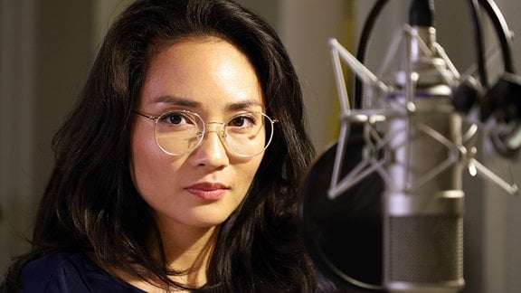 Mai Duong Kieu, eine Frau mit Brille steht vor einem Mikrofon