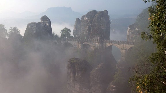 Nebel zieht über die Basteibrücke nahe Lohmen in der Sächsischen Schweiz, im Hintergrund ist der Lilienstein zu sehen
