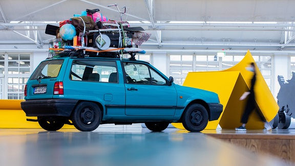 Kunstinstallation "Nowhere is Home", ein hellblaues Auto mit Gepäck auf dem Dach