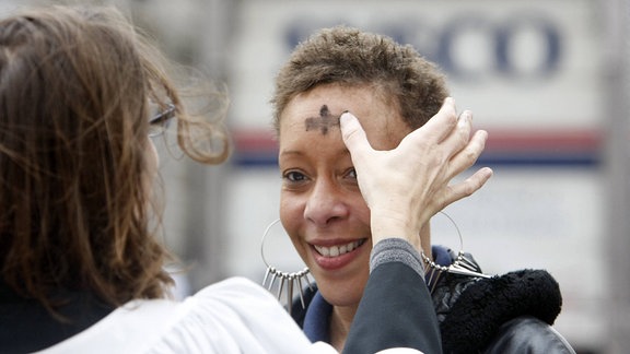 Einer jungen Frau wird ein schwarzes Kreuz auf die Stirn gemalt