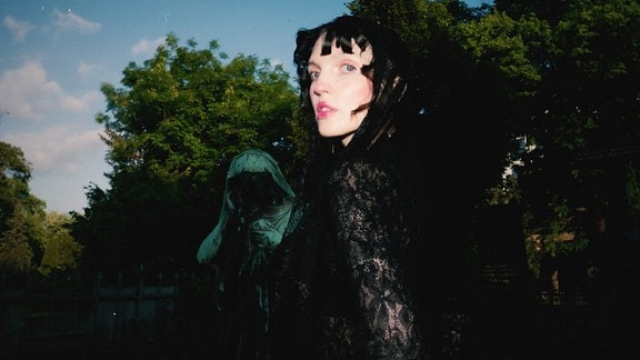 Mia Morgan komplett im schwarzen Gothic-Look nur halb der Kamera zugewendet