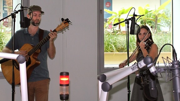 Ein Mann mit Gitarre und eine Frau mit Geige spielen in einem Hörfunkstudio