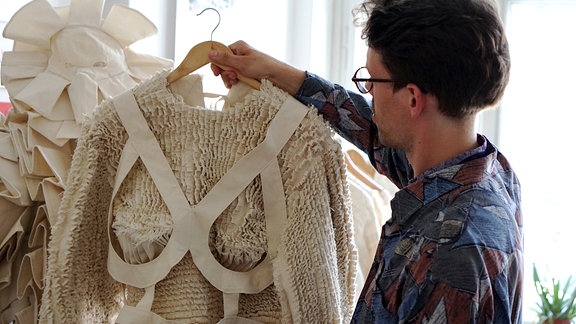 Modedesigner Kaur Hensel hält Kleidungsstück