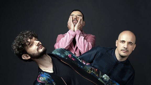 Die drei Bandmitglieder von  Moderat vor dunklem Hintergrund