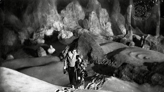 Szene aus Frau im Mond - Ein Mann und eine Frau laufen auf der Mondoberfläche entlang.