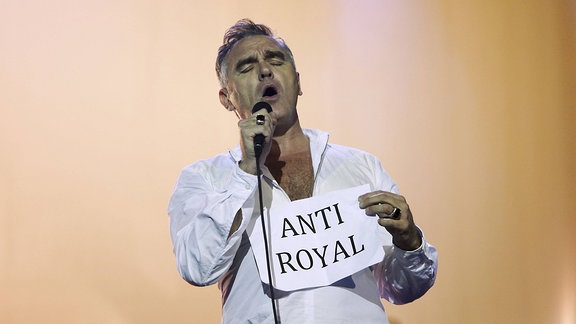 Bei einem Konzert hält Morrissey ein Blatt Papier hoch, auf dem "Anti Royal" steht.