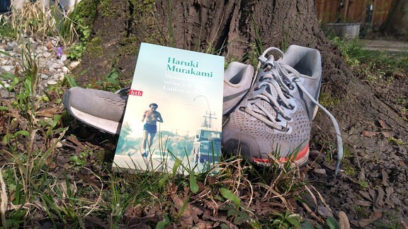 Auf Laufschuhen liegt das Buch "Wovon ich rede, wenn ich vom laufen rede" von Haruki Murakami