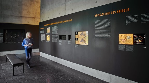 Blick in die Ausstellung im Museum Lützen 1632, dunkle Tafeln auf einer grauen Betonwand, im Hintergrund eine Frau