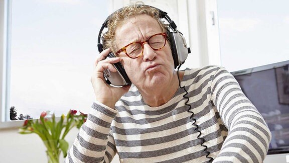 Ein älterer Mann sitzt in seinem Wohnzimmer und hört Musik über Kopfhörer.