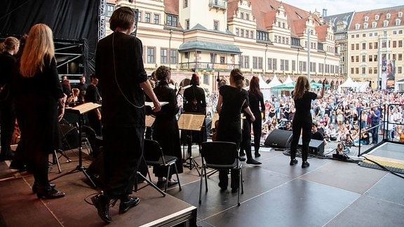 Blick von einer Konzertbühne, auf der Sängerinnen in schwarzer Kleidung stehen, ins Publikum auf den Leipziger Marktplatz, im Hintergrund historische Gebäude.