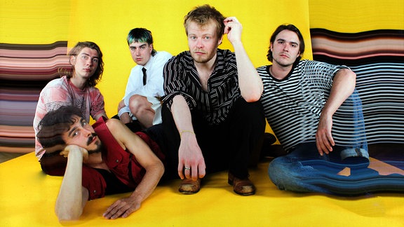 Die fünf Musiker der Band Buntspecht posieren gemeinsam im Sitzen vor einem gelben Hintergrund.