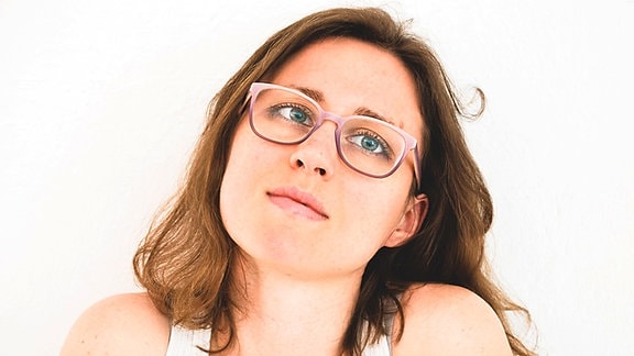 Porträt einer jungen Frau mit welligen hellbraunen Haaren und einer Brille.