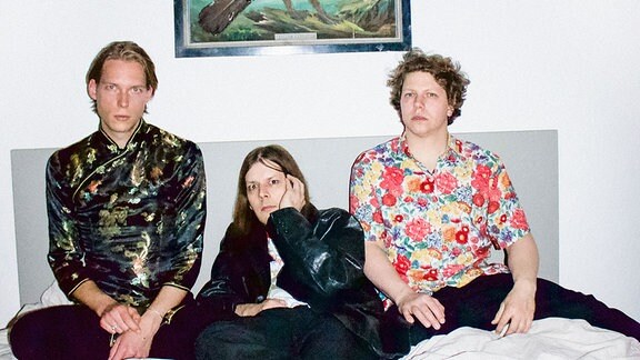 Die drei Musiker der Band Die Nerven sitzen auf einem Bett.