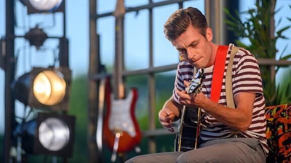 Ein Mann sitzt auf einer Bühne und spielt Gitarre