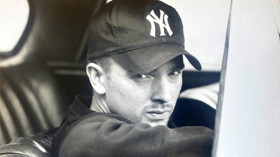 Schwarz-Weiß-Foto eines jungen Mannes in einem US-Car mit einer New York Yankees Kappe